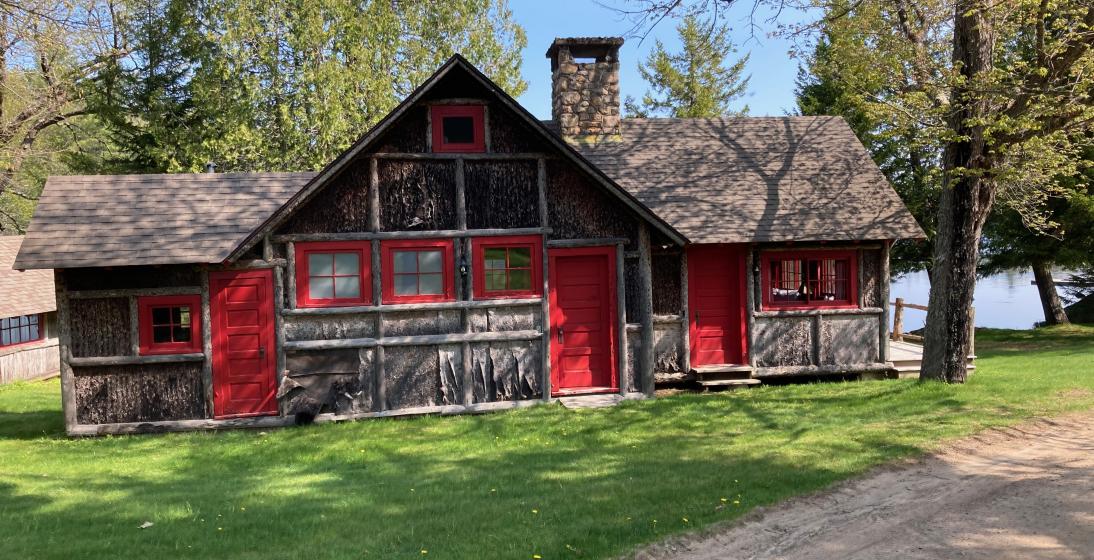 A wood cabin with rustic red trim on the sides with a green yard surrounding it. 