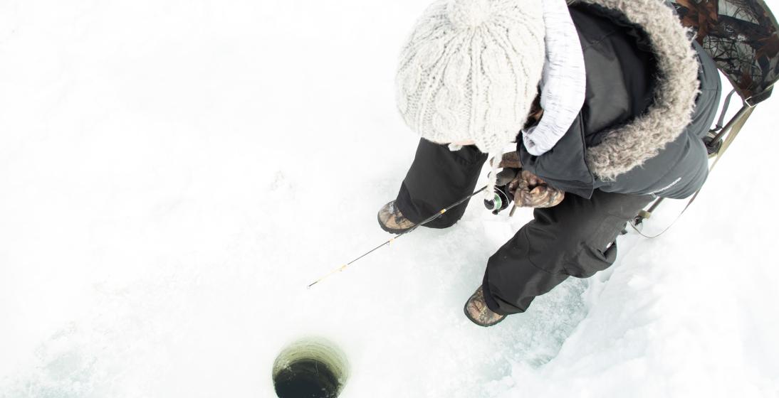 An angler sinks their line down a hole in the ice