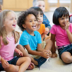 Children of pre-k age sitting on the floor enjoying a story read to them