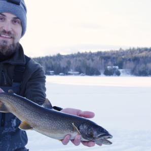 A man holding a fish he caught while ice fishing