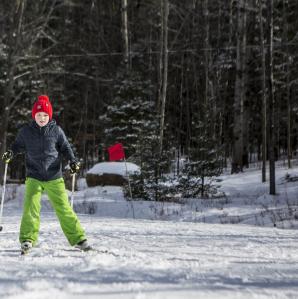 A boy with a red winter hat, black winter coat, and lime green snowpants, is cross-country skiing