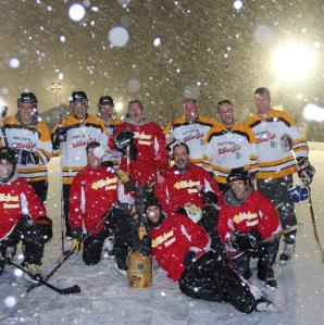 Two teams of hockey players posing for a photo on the ice with snow falling