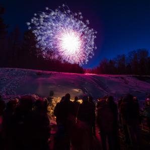 fireworks above a group of people around a bon fire