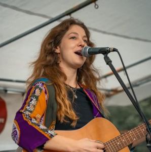 A photo of Jessie singing into a microphone and playing her guitar