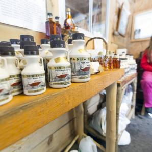 Girl sitting at the end of a table with many maple syrup bottles for sale