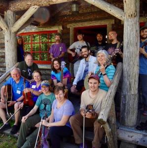 Group of people sitting and standing on the porch at Great Camp Sagamore holdong their instruments