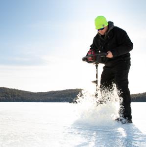 Man using an ice auger on a frozen lake.