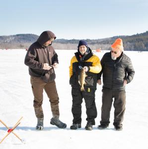 Three men holding a fish on a frozen lake.