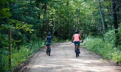 Two cyclists bike down a dirt road