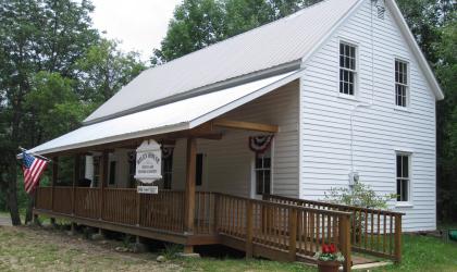 The exterior of a small white building with a wooden ramp.