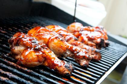 Several pieces of chicken covered in bbq sauce grilling on a black grill rack