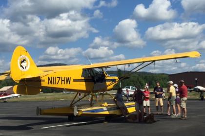 A yellow small plane parked at the airport with several people standing around it looking at it.