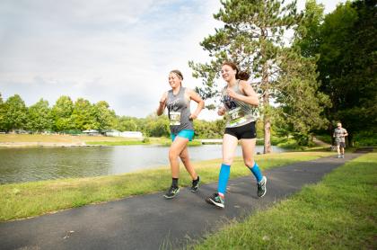 Two girls running in a race&#44; on a path with a creek beside the path on a nice day in the summer 