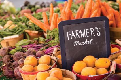 A photo of several baskets filled with various fruits and veggies with a chalk board sign which reads Farmer's Market