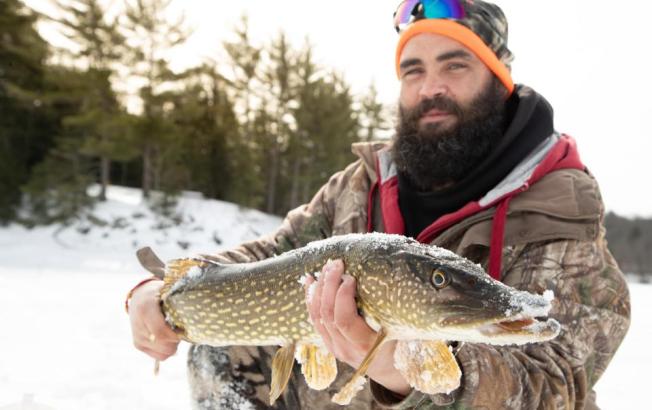 A man holding a fish caught from ice fishing with a snowy background.