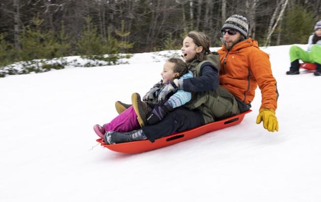 A family of three all fit onto one sled and slide down a hill.