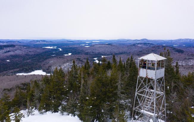 A fire tower in winter over the tree tops.