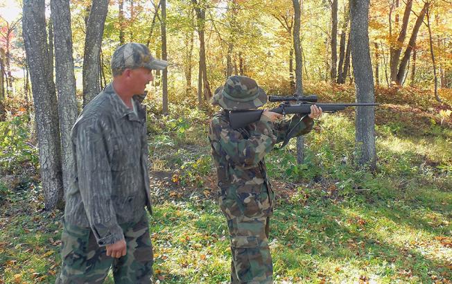 A woman shoots a rifle into the woods.