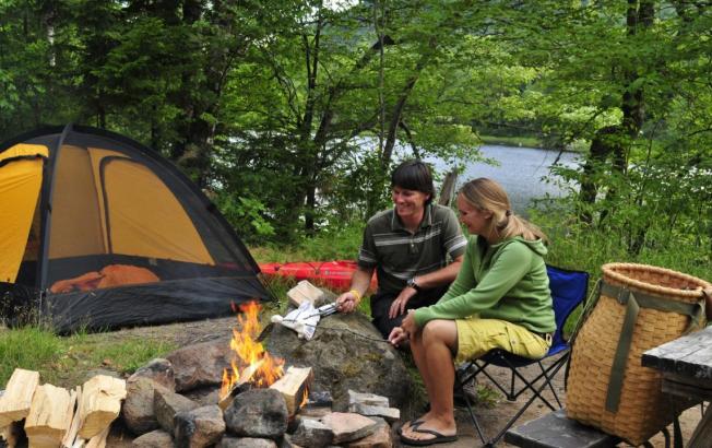 a man and woman roast marshmallows at a campsite.