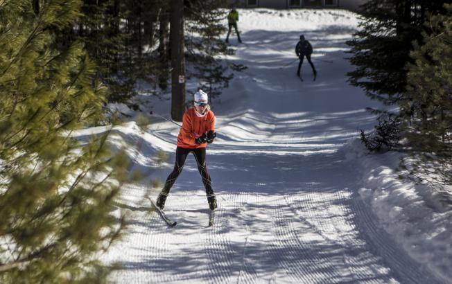 A woman and two other skiers ski down a snowy path.