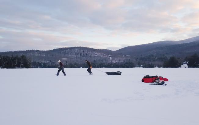 Two people pull a sled over the ice