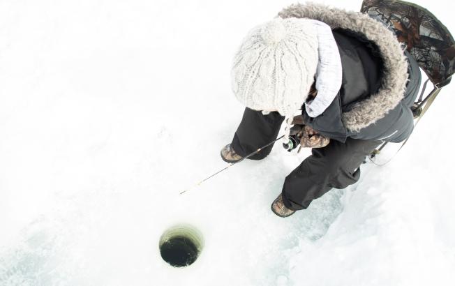 An angler sinks their line down a hole in the ice