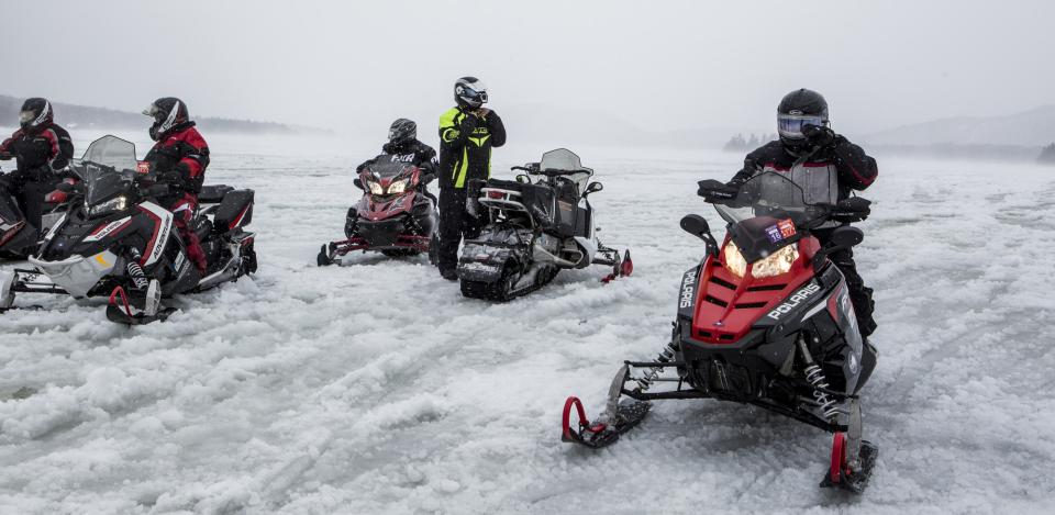 A group of snowmobilers on a snowy lake.