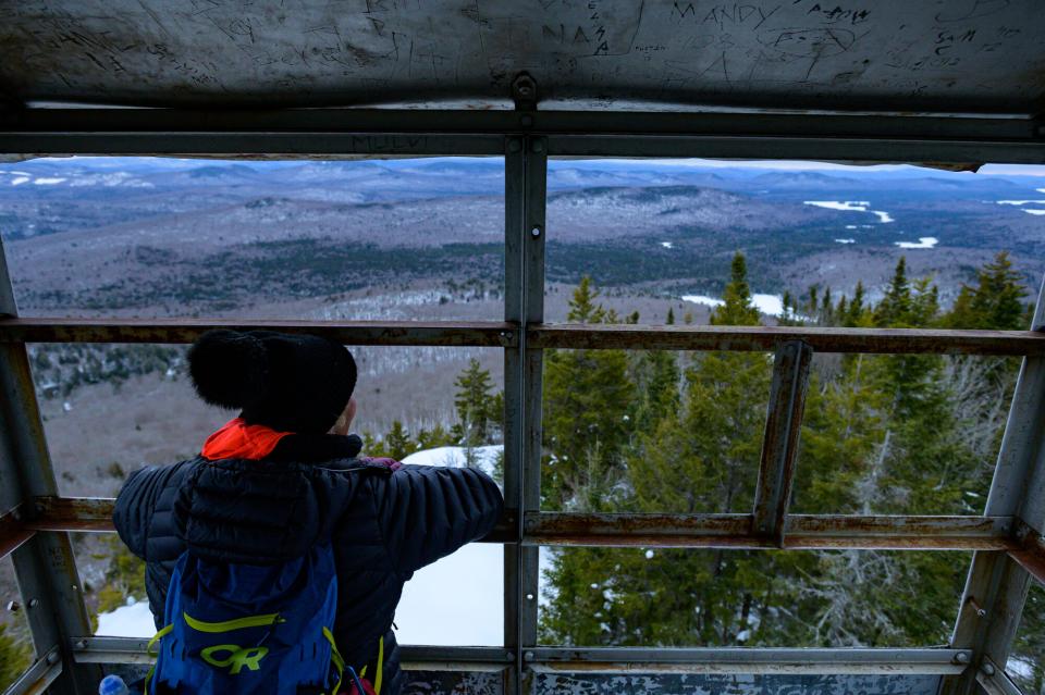 A woman looks out at the snowy view from inside a metal firetower