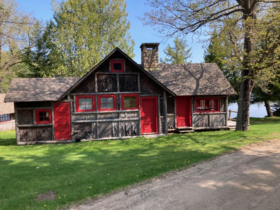 A wood cabin with rustic red trim on the sides with a green yard surrounding it.