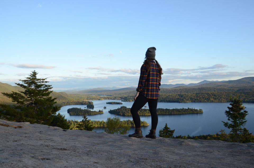 A woman stands on top of castle rock mountain surrounded by wilderness.