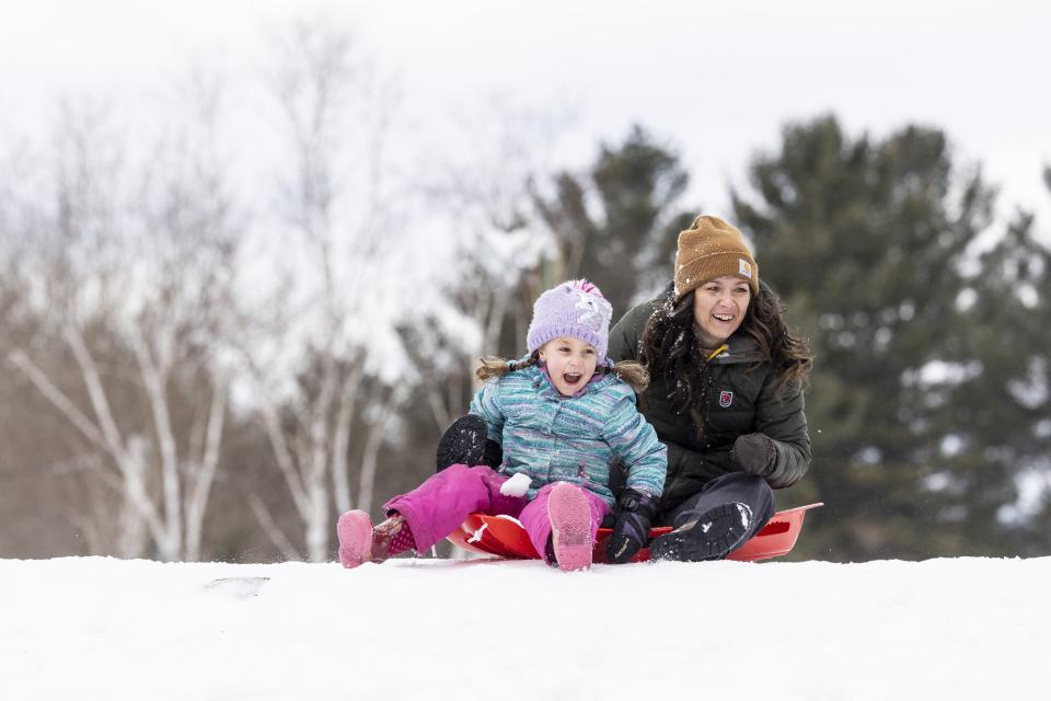 A woman and young girl sled down a hill in winter.