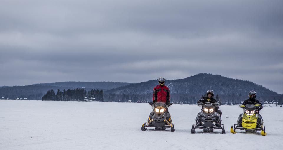 Three snowmobilers in the snow with headlights on.