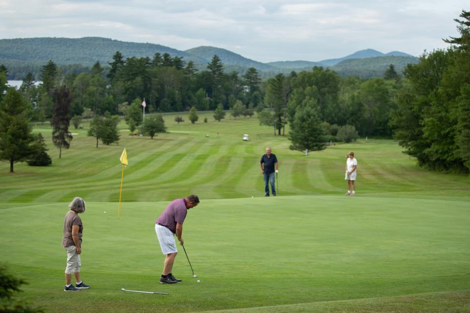 Golfers take a swing on the green with mountain views in the background