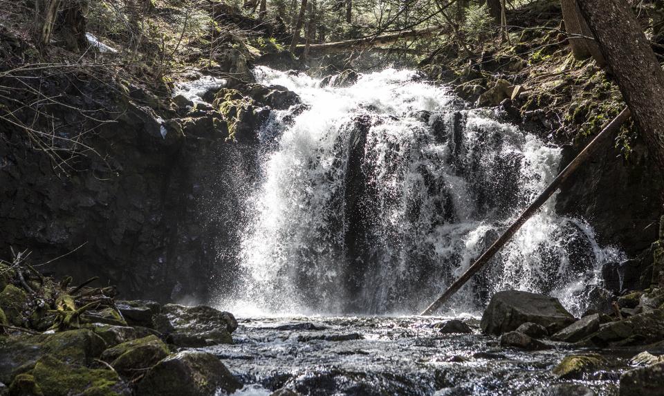 falls spill over a rock ledge into a rushing stream.