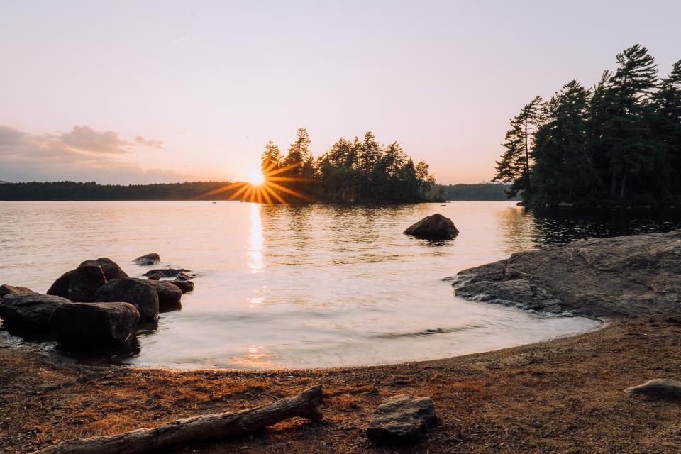 The sun sets behind a small island and over a lake tinged pink and orange by the light.