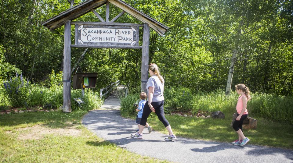 A woman and two children walk toward a wooden arch for a community trail.