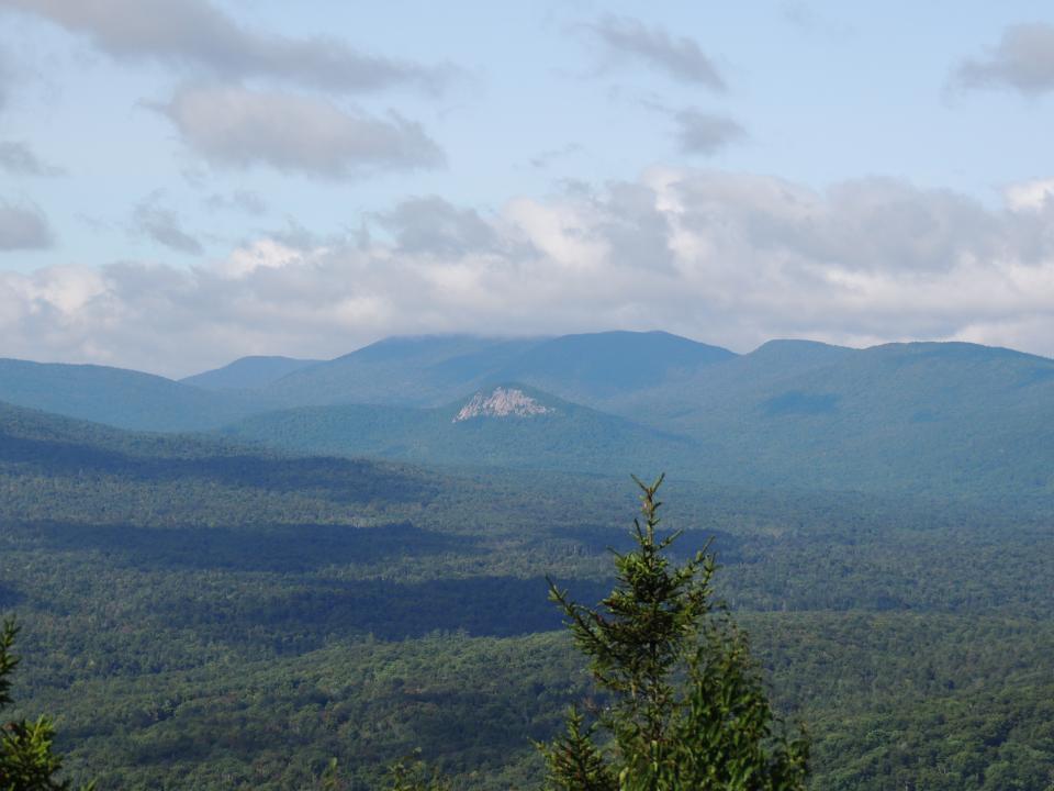 A view of forested mountains from the summit of a mountain.