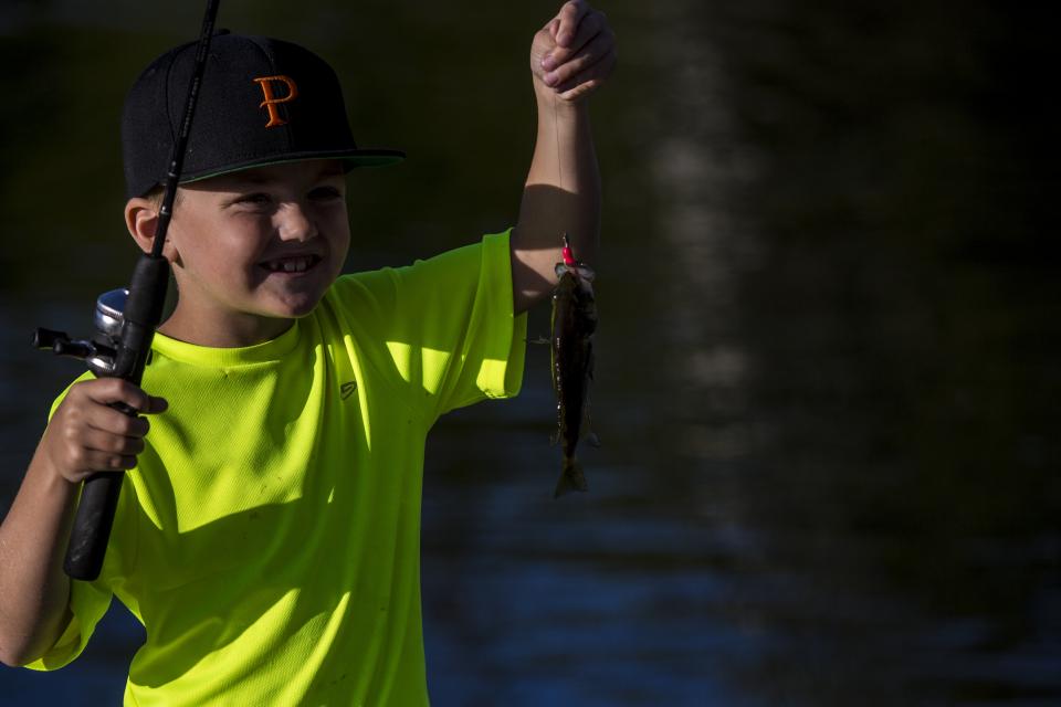 A child holds up his catch of a fish.