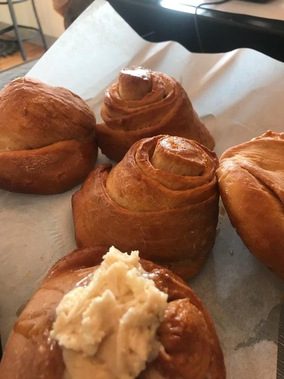 Freshly baked cinnamon buns cool off on a baking sheet before getting frosted