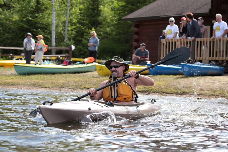 A man paddles a kayak away from a shoreline lined with beached kayaks.