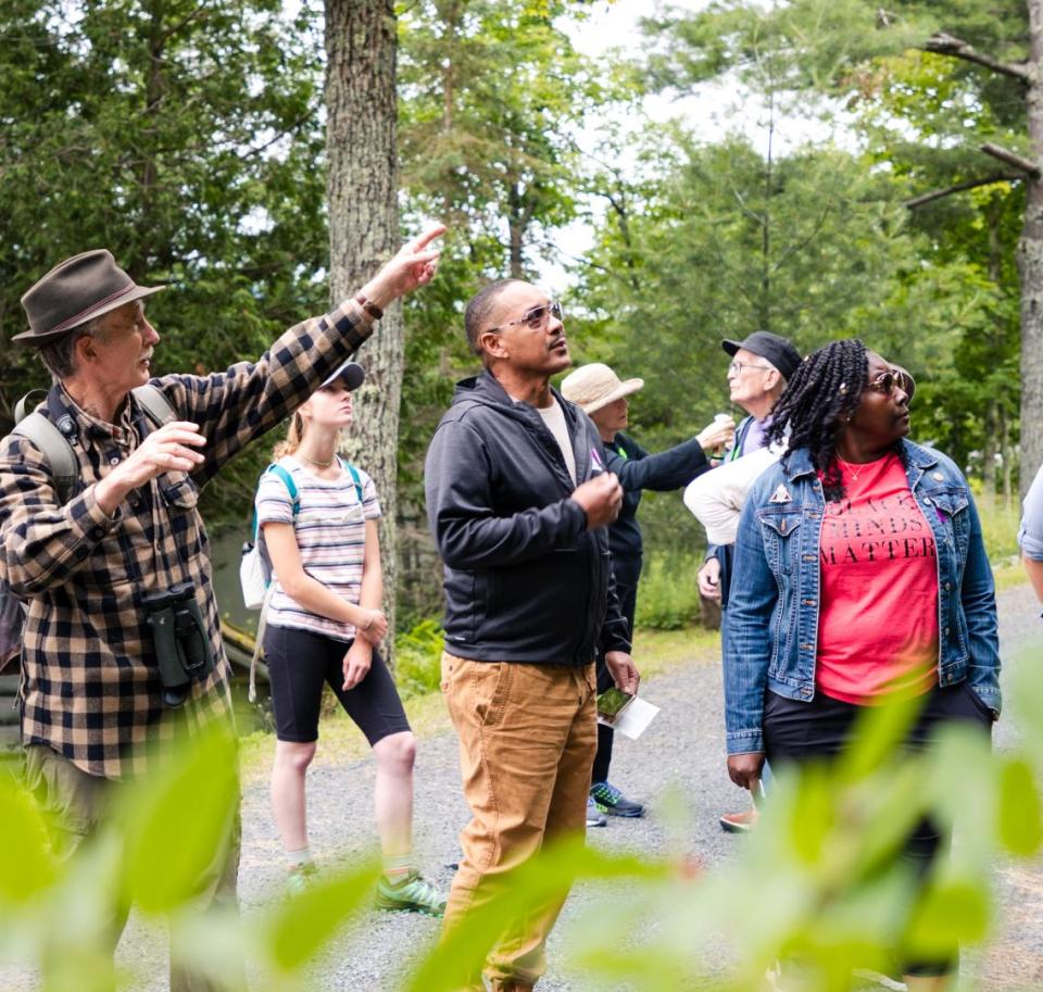 An older man points to the trees to a tour group.