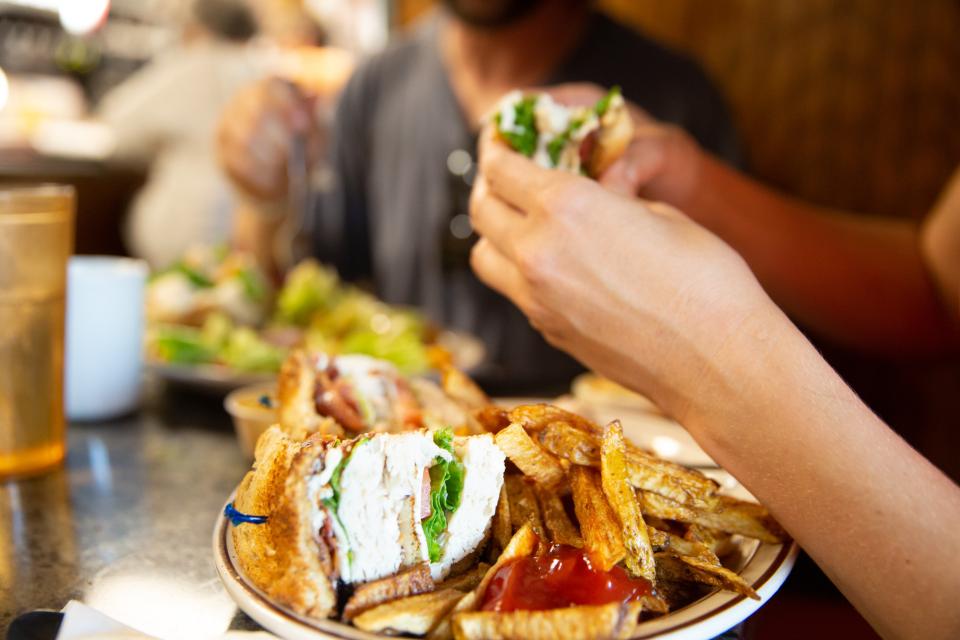 A woman eats a turkey club sandwich with fries.