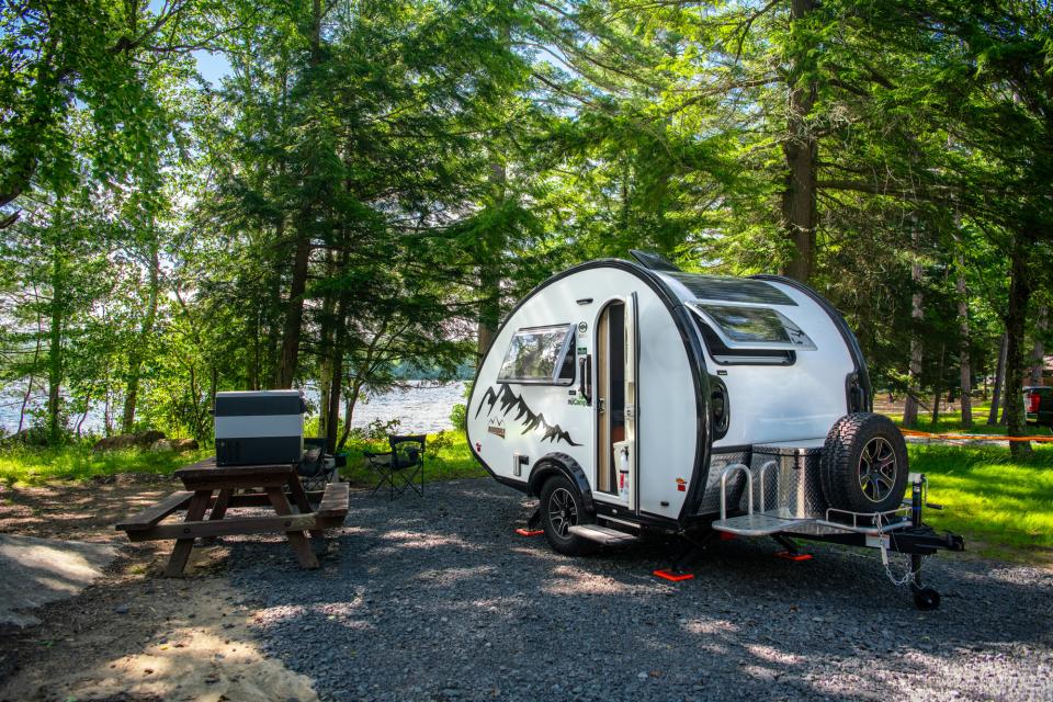 A round camper parked at a campsite with picnic table and folding chairs.