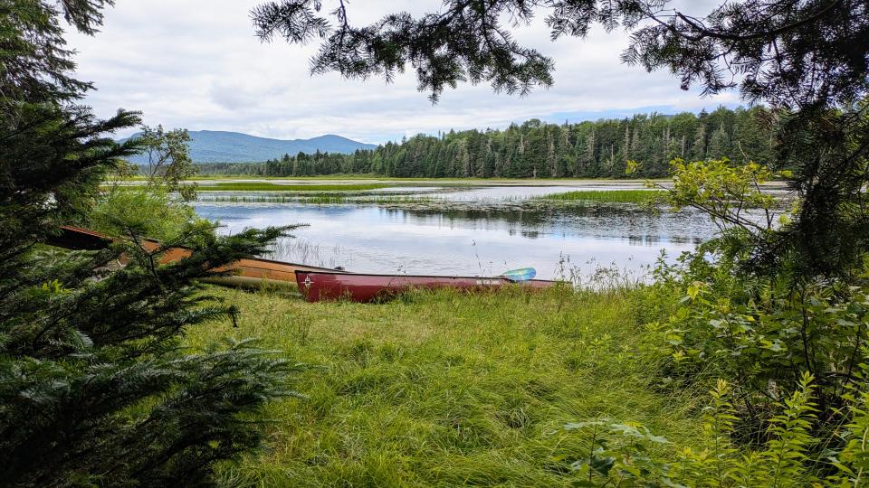 Canoes in the grass along the edge of the water with mountains in the background