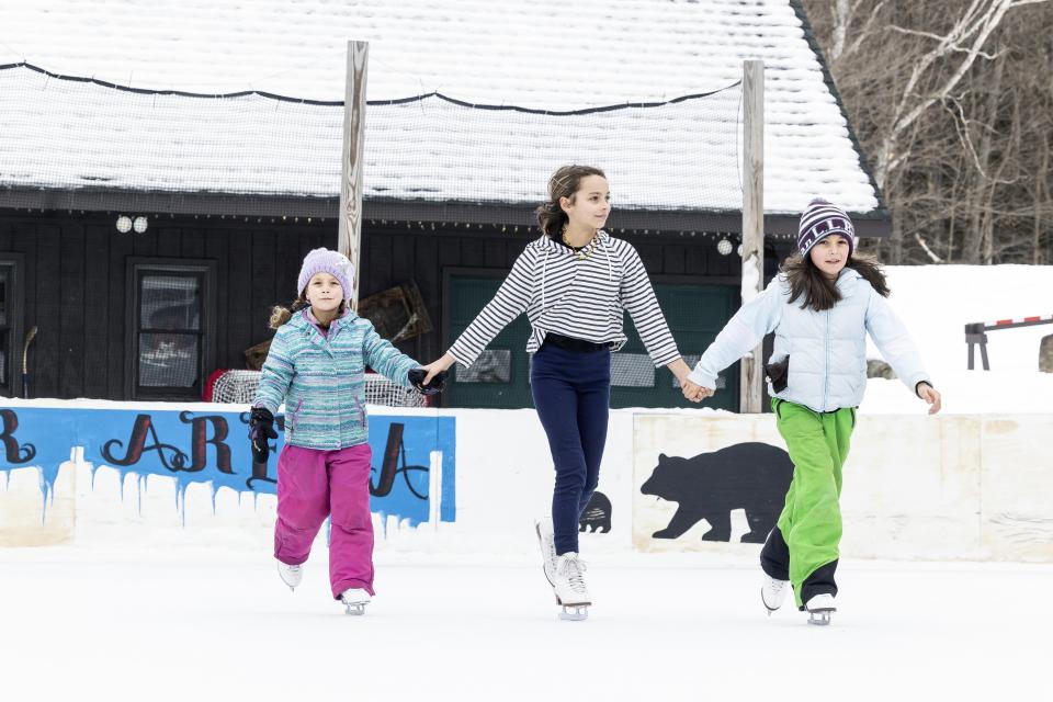 3 ice skaters holding hands on the rink.