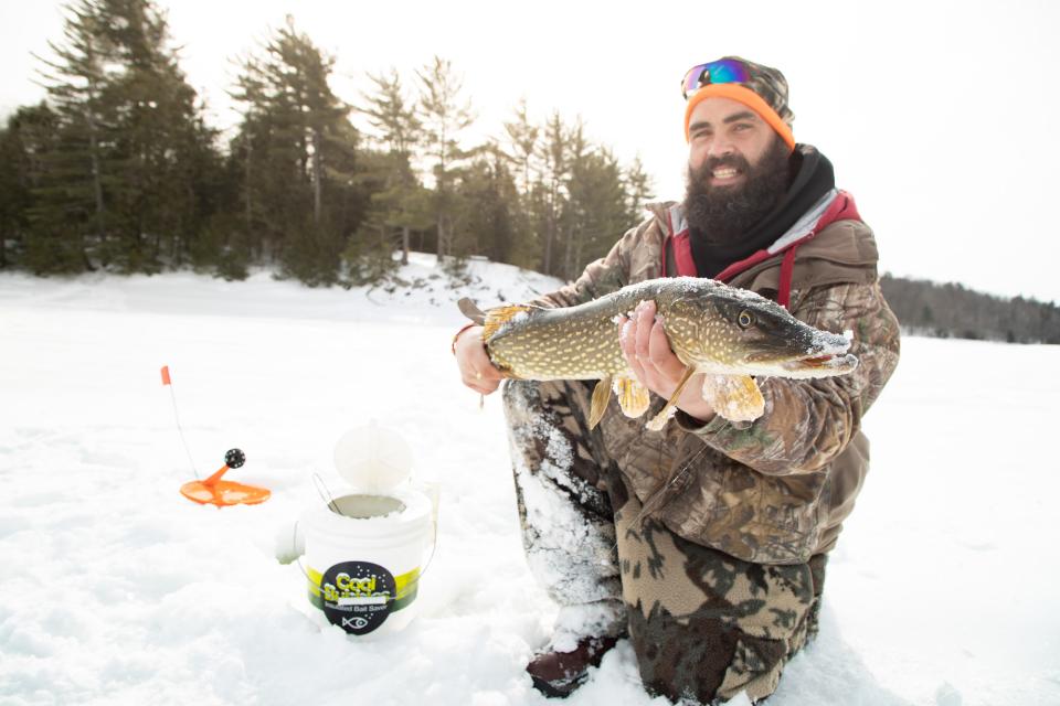 A man holds up a fish he caught on the ice of a lake.