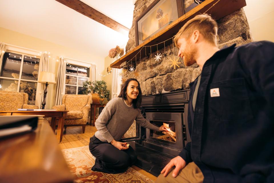 A man and woman feed a fireplace in a cottage.