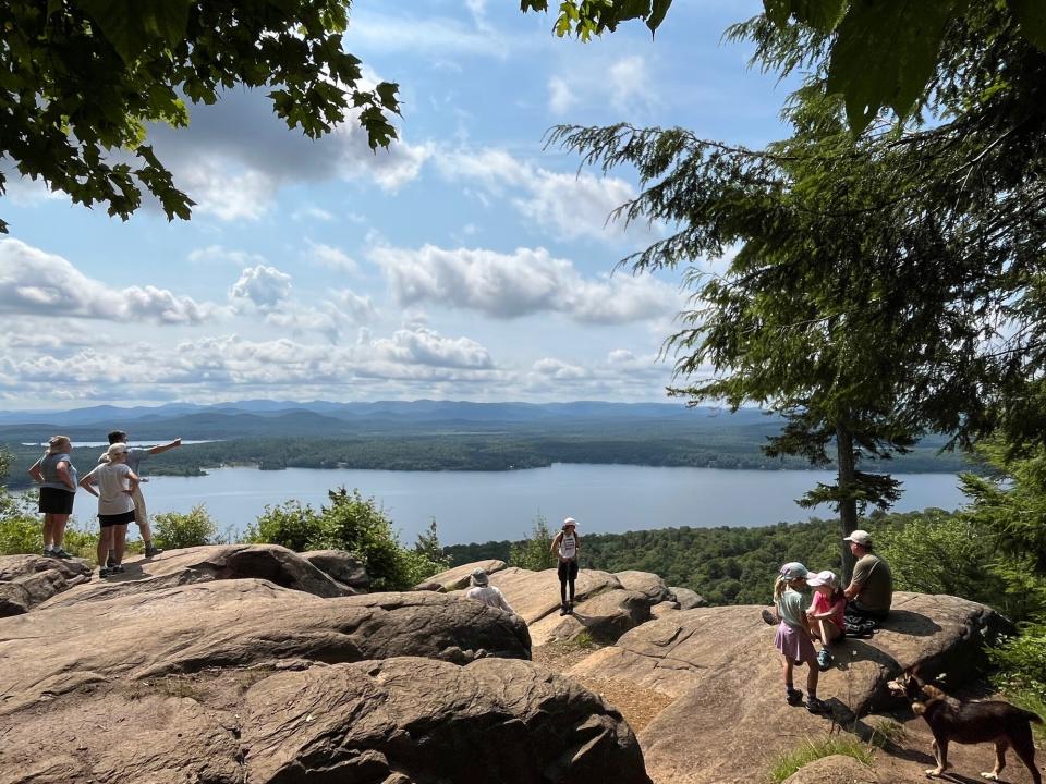 People stand on top of a rocky mountain top overlooking a lake.