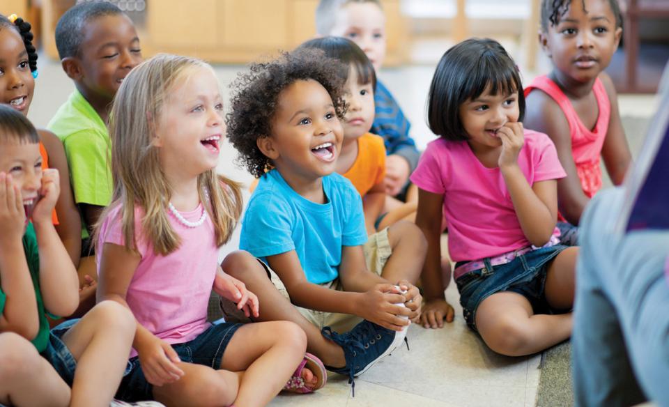 Children of pre-k age sitting on the floor enjoying a story read to them