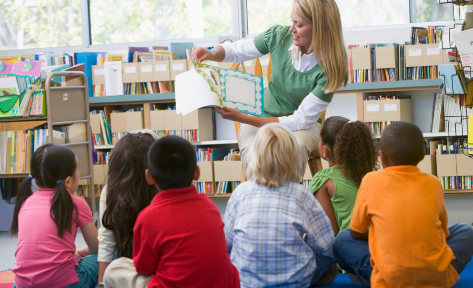 Children sitting on the floor enjoying a story read to them by a woman sitting in a chair